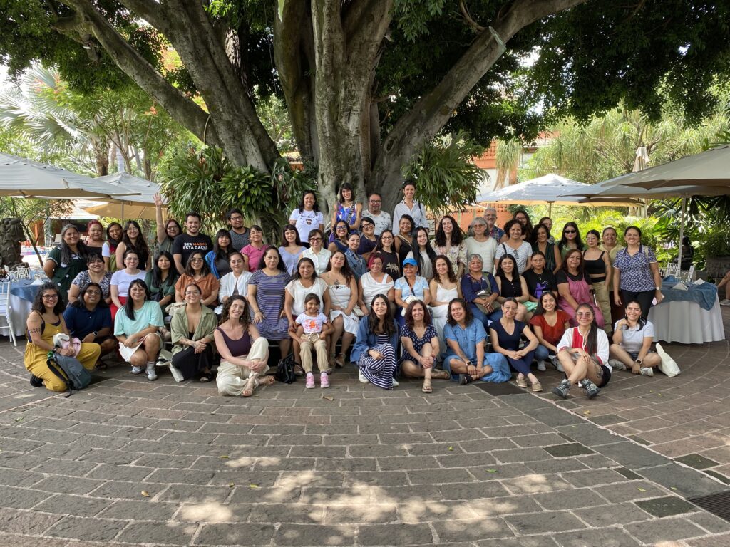 Fotografía de grupo de les integrantes del encuentro frente a un árbol en una explanada